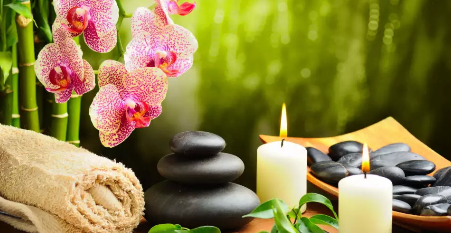 Image of Hot stone massage setting lit by candles - Towel on fern with candles and black hot stone on green background.